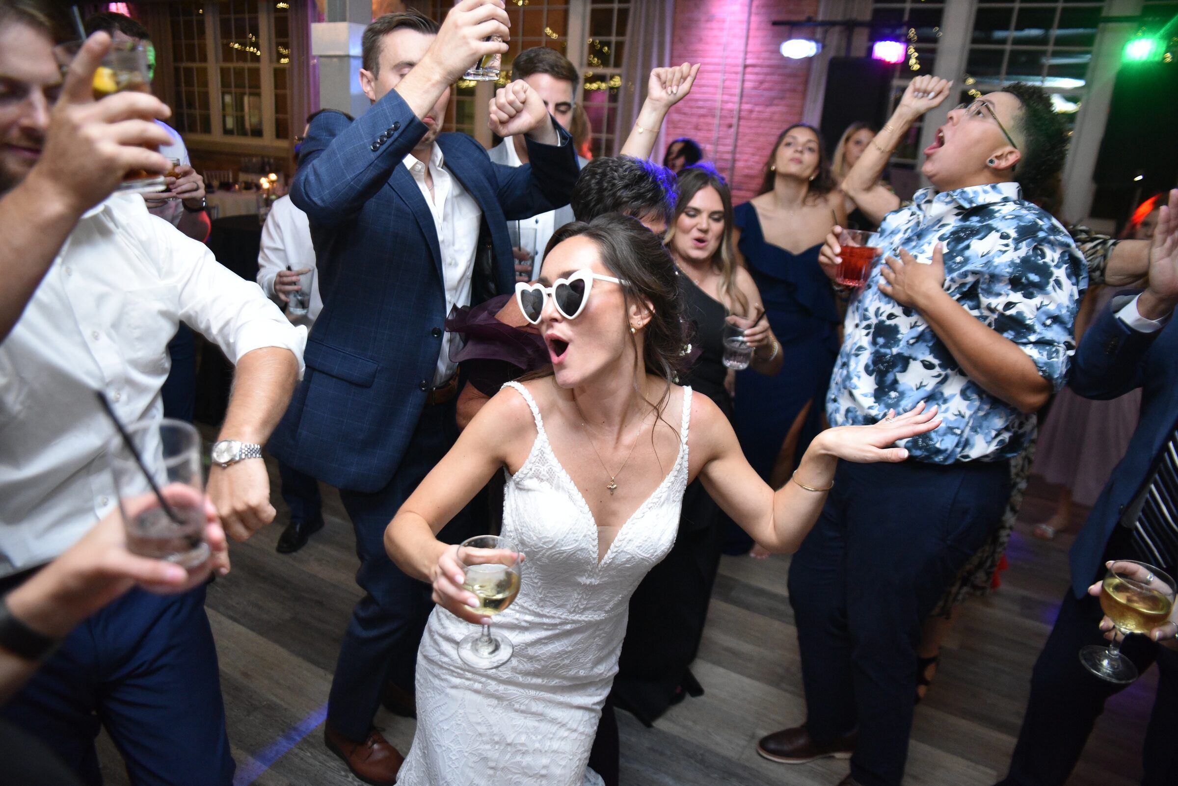 Bride in heart-shaped sunglasses dancing with guests on the dance floor