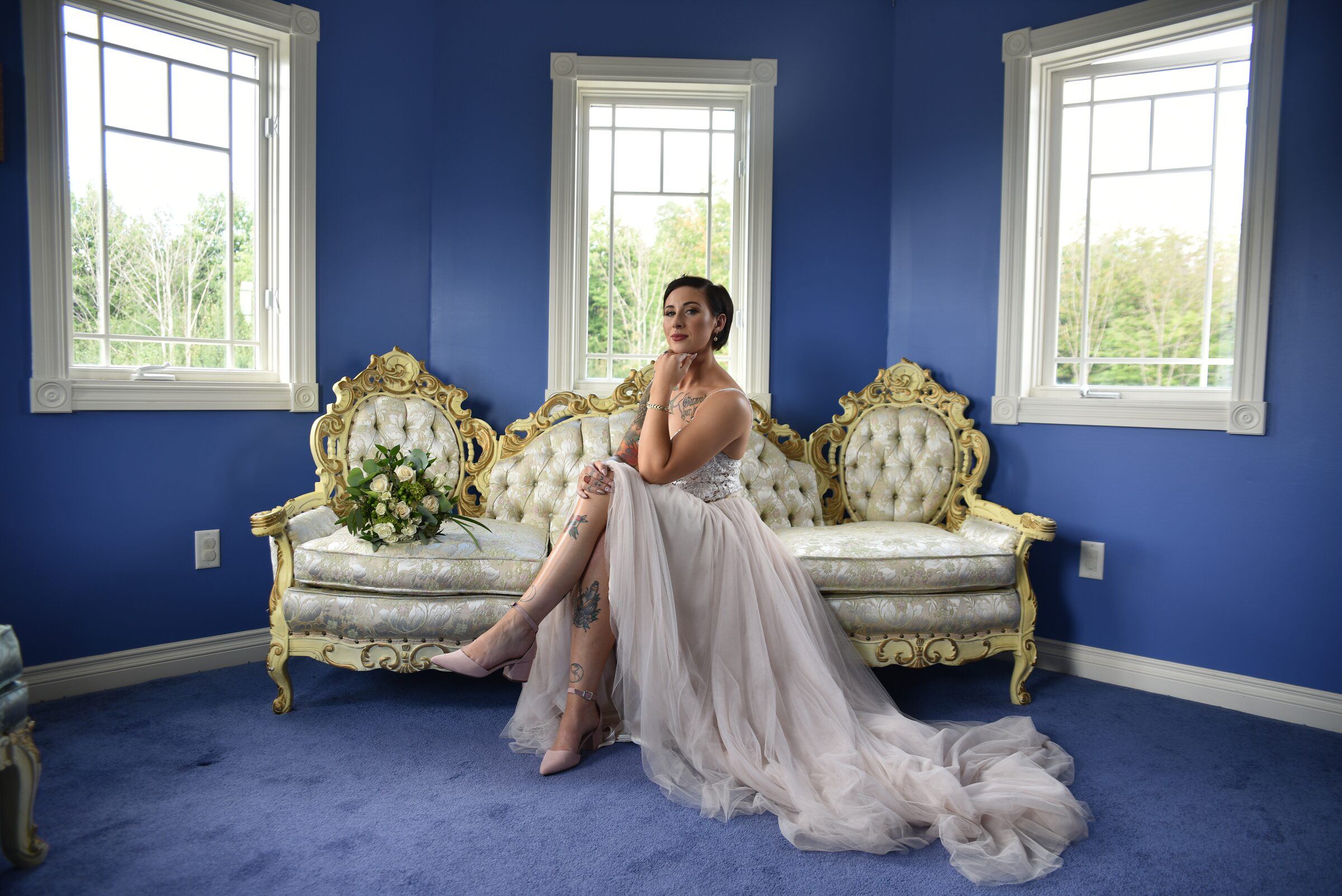 Bride posing with a bouquet on a gold vintage sofa in a blue room