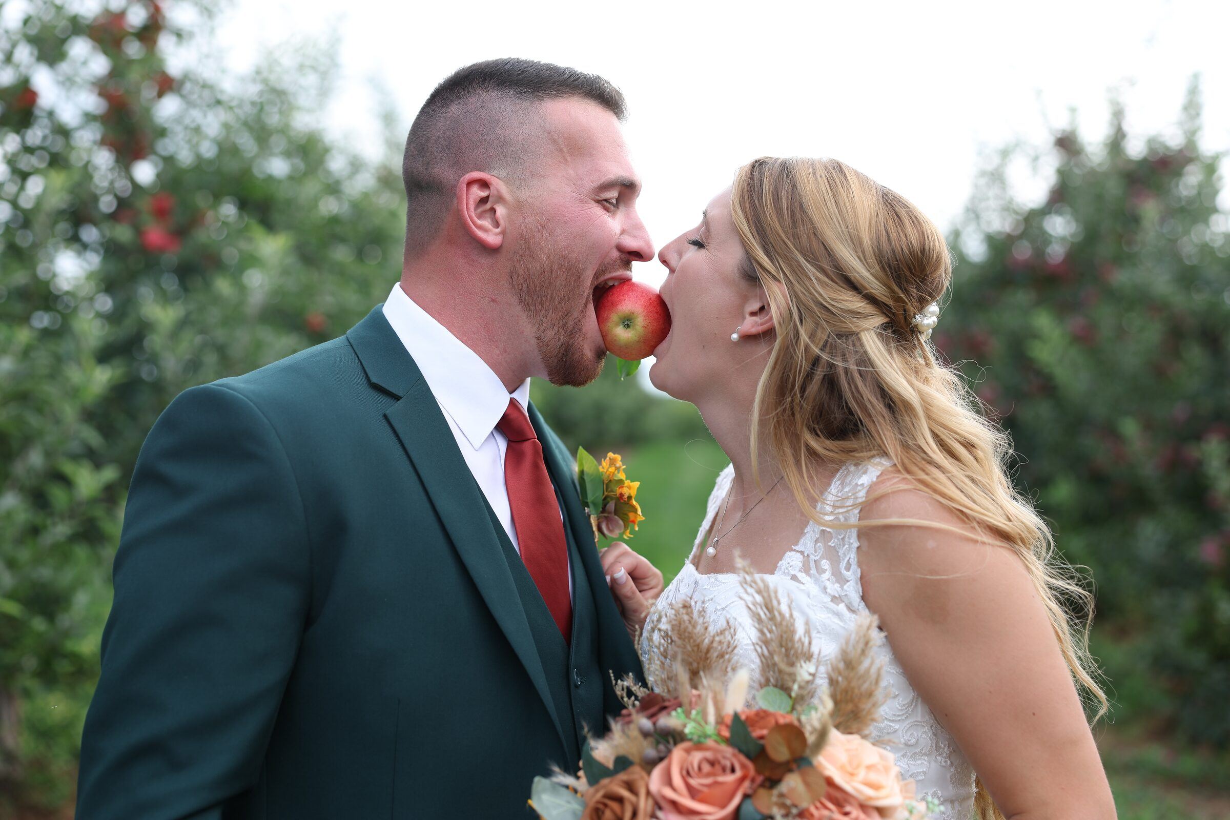 Bride and groom bite the same apple in an orchard
