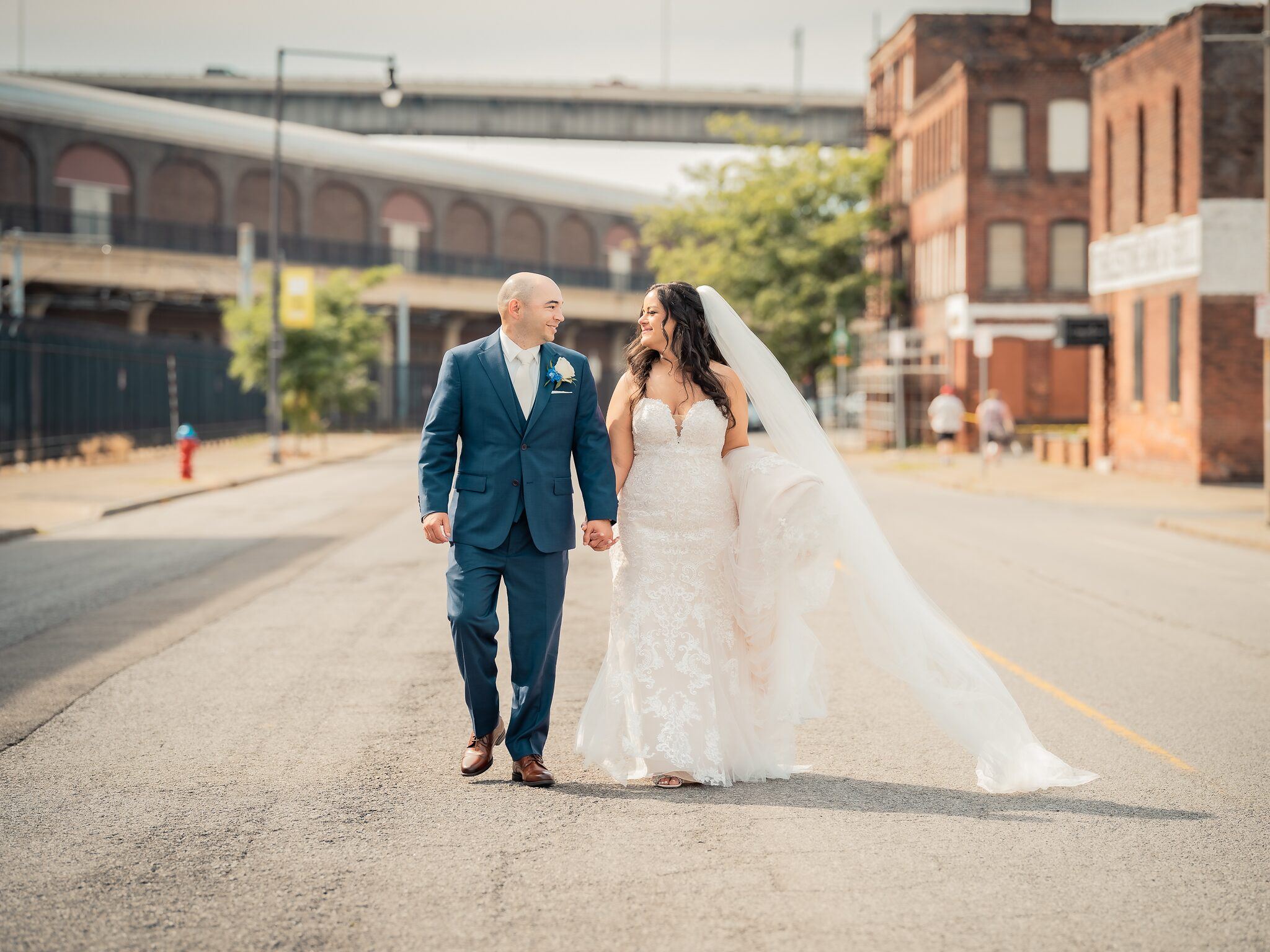Bride and groom walk hand in hand down an empty city street lined with brick buildings