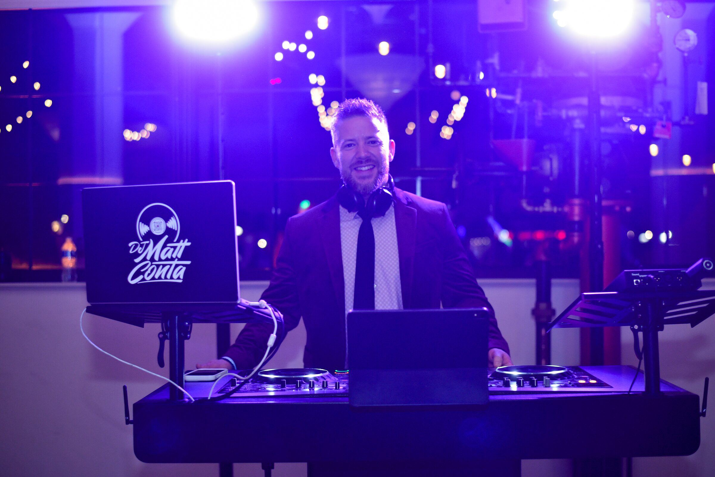 DJ behind his controller and laptop with bright purple lighting behind him