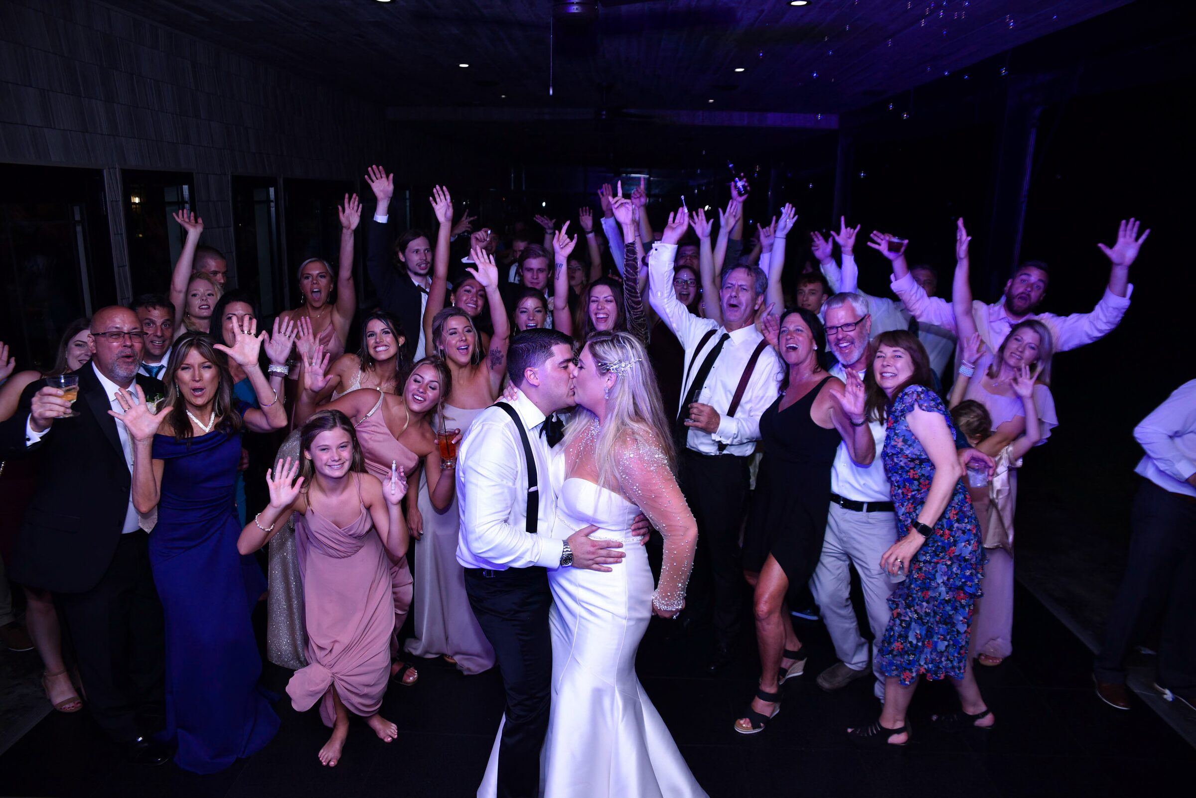 Couple kisses while guests surround them with arms raised on a packed dance floor