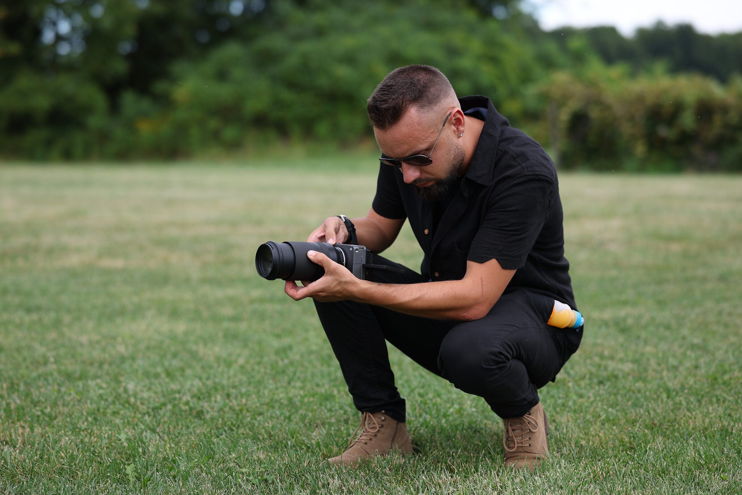 Wedding photographer crouching in a grassy field to adjust his camera